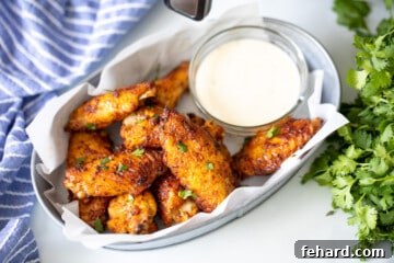A serving basket overflowing with delicious Air Fryer Chicken Wings, positioned next to the sleek air fryer that made them.