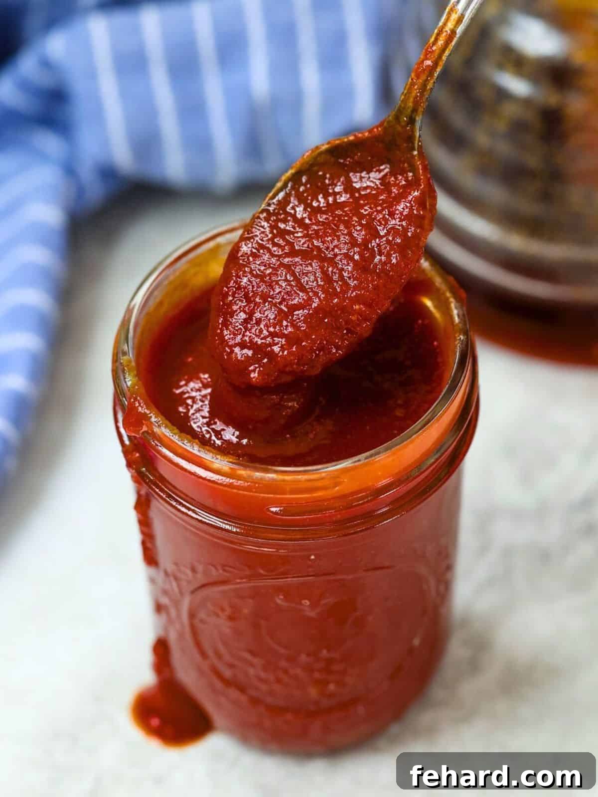 Best Homemade Barbecue Sauce A glass jar filled with rich, dark homemade BBQ sauce, with a wooden spoon dipped inside.