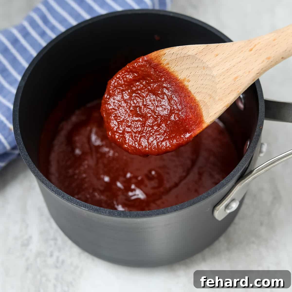 Thickening the Ketchup-Free BBQ Sauce A wooden spoon stirs thick, simmering homemade barbecue sauce in a stockpot.