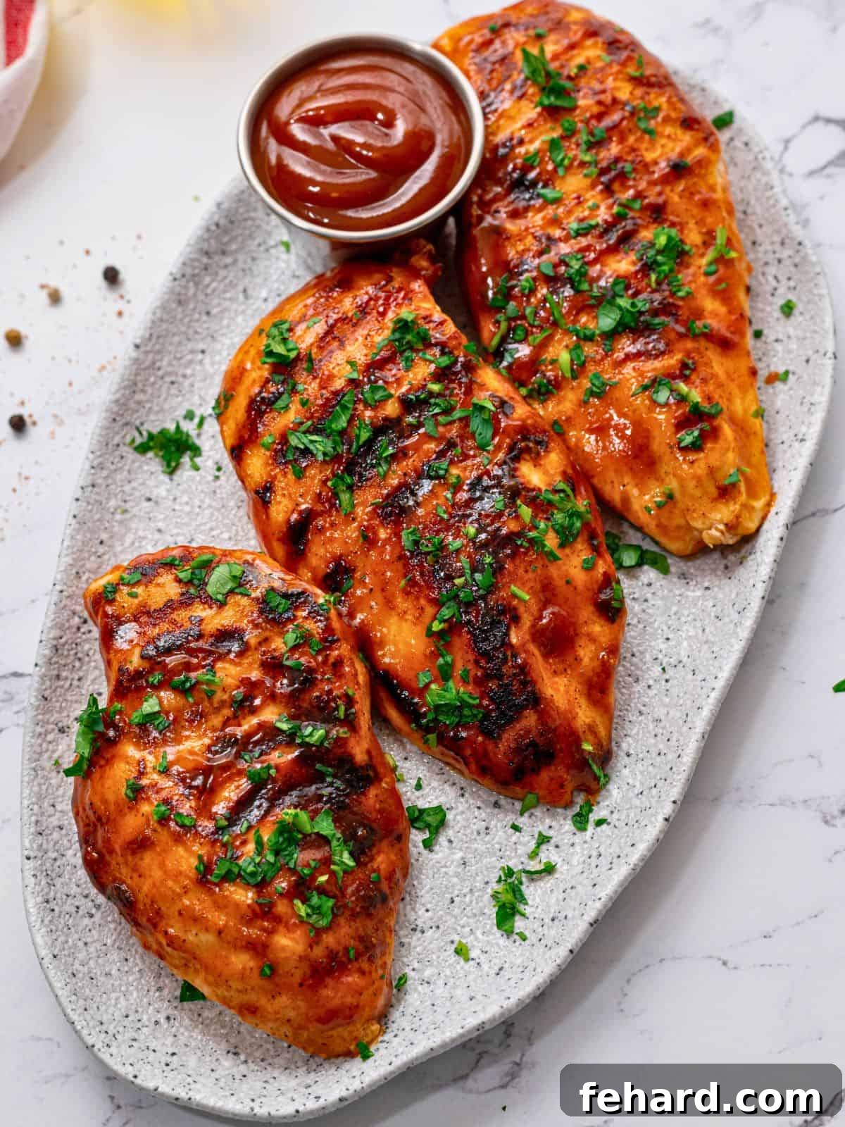 Three juicy, tender grilled barbecue chicken breasts on platter basted with BBQ sauce and topped with parsley.