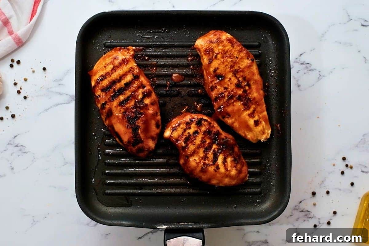 Three chicken breast on grill plate that have been grilled and basted with barbecue sauce.