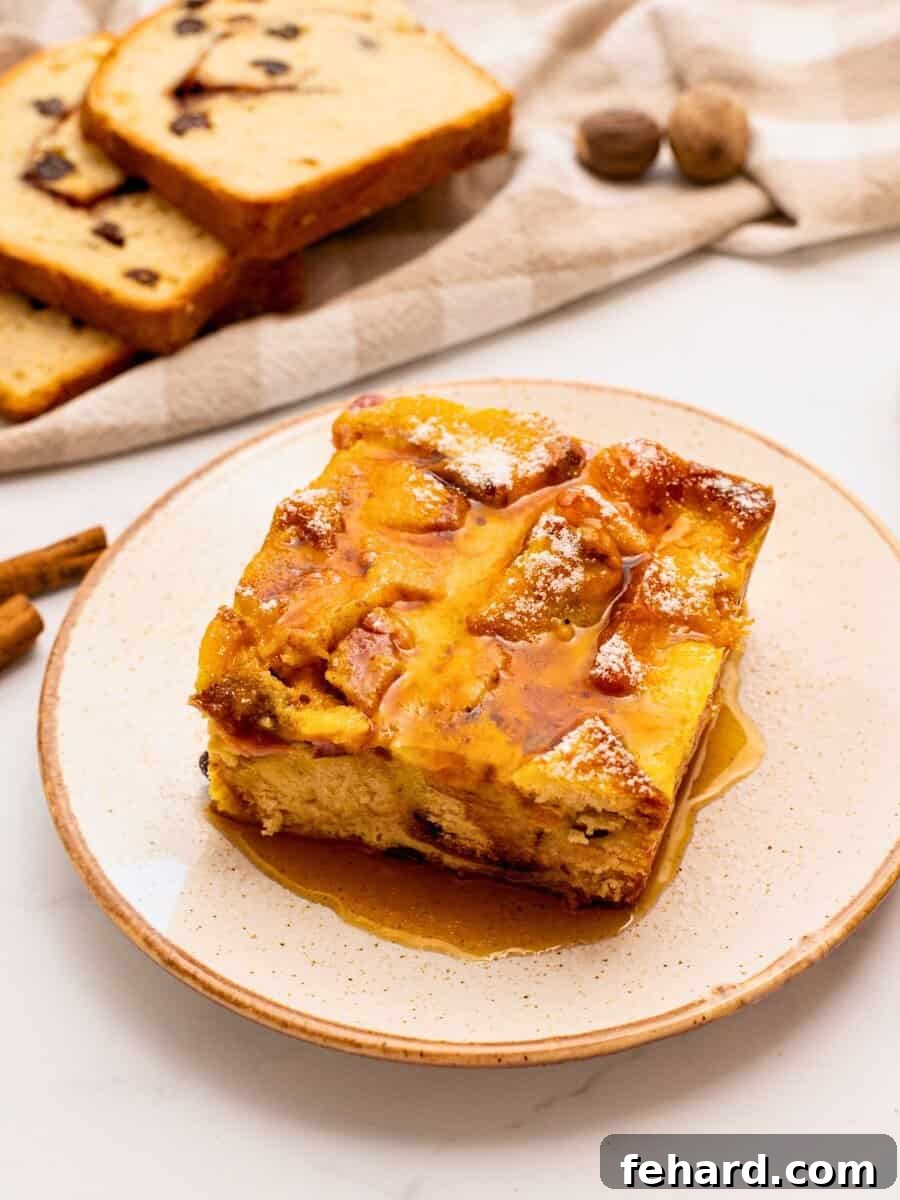 A glorious slice of overnight breakfast casserole made with cinnamon raisin bread, eggs, cubed ham, sharp cheddar cheese, and a light drizzle of maple syrup and dusting of powdered sugar on top, served on a white plate.