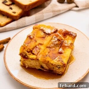 Slice of overnight breakfast casserole made with cinnamon raisin bread, eggs, cubed ham, sharp cheddar, and eggs on plate topped with maple syrup and powdered sugar.