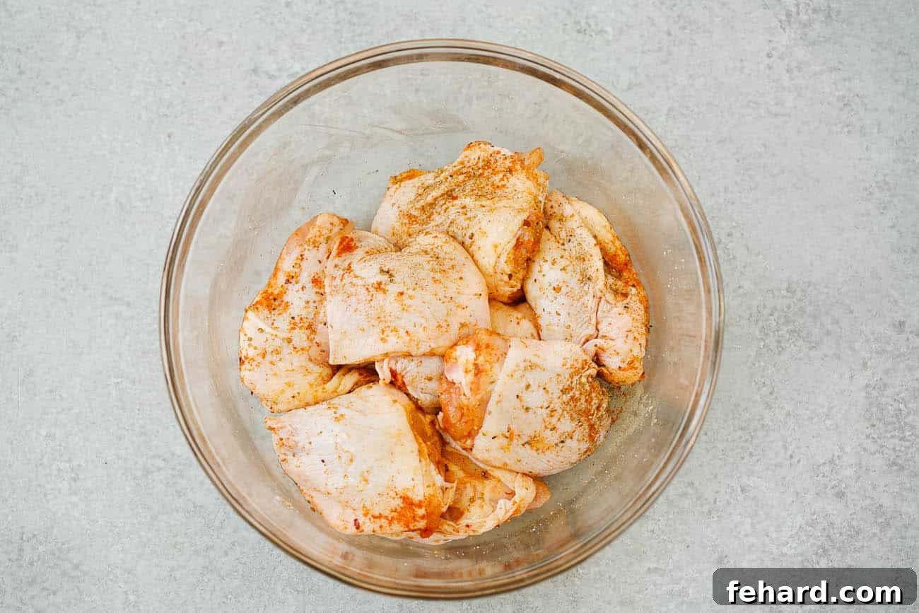Crispy Air Fryer Chicken Thighs 5 Overhead view of raw boneless, skin-on chicken thighs in a large glass bowl, coated with a generous layer of seasoning.