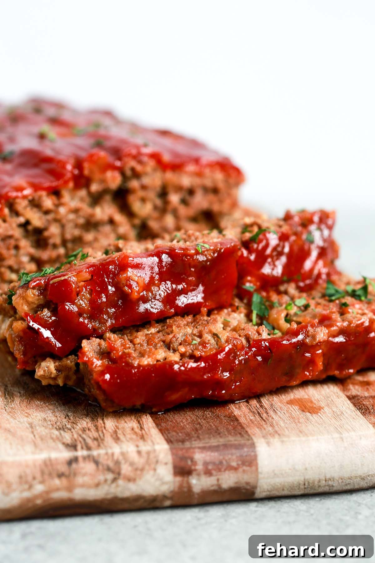 Guilt Free Meatloaf Perfection 2 slices of homemade meatloaf with tomato sauce on top on cutting board