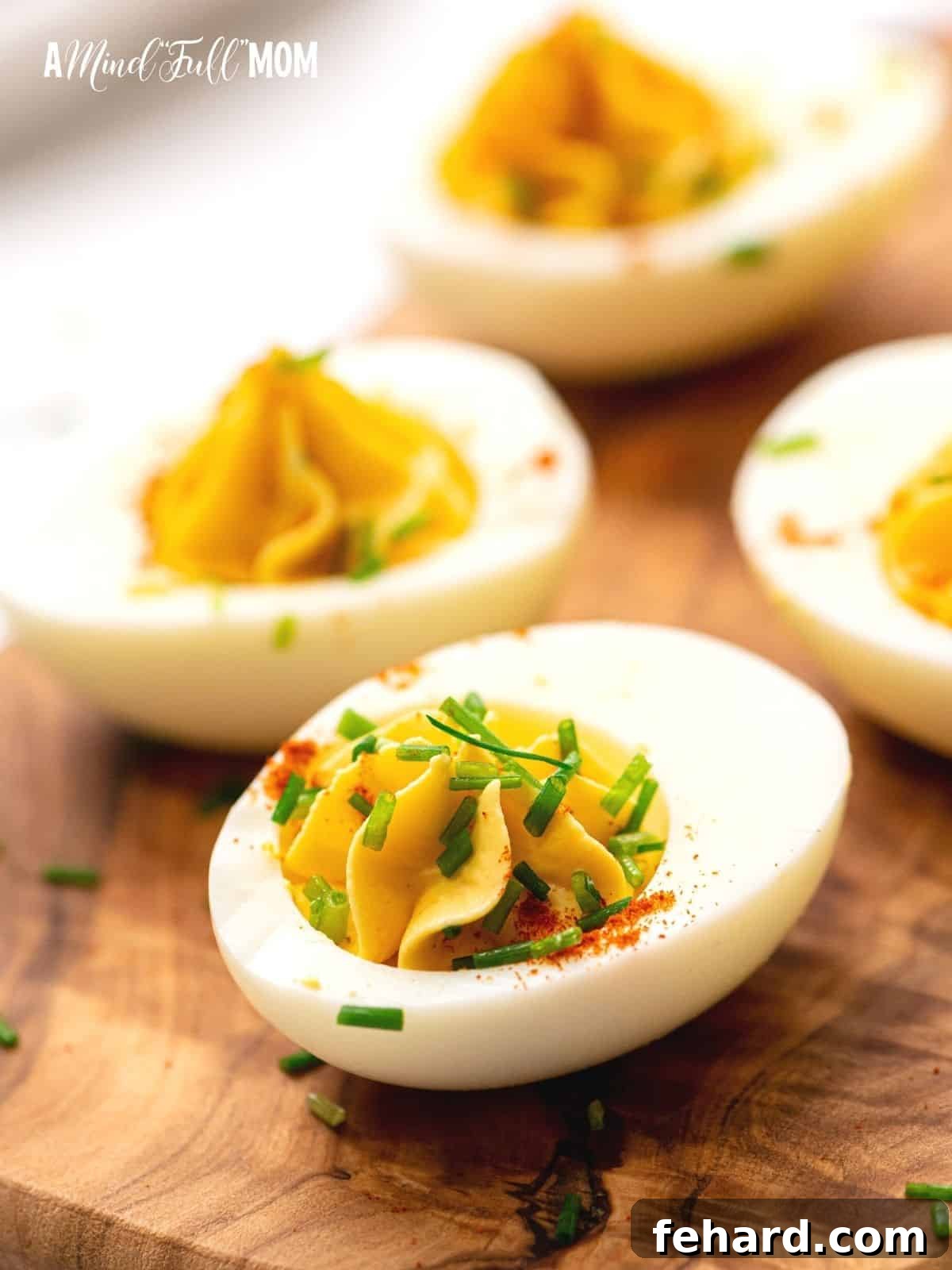 Perfect Deviled Eggs Recipe Exquisitely arranged deviled eggs, garnished with fresh chives, on a rustic wooden cutting board, ready to be served.
