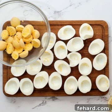 Irresistible Deviled Eggs 5 Hard boiled eggs cut in half with whites on cutting board and yolks in mixing bowl.