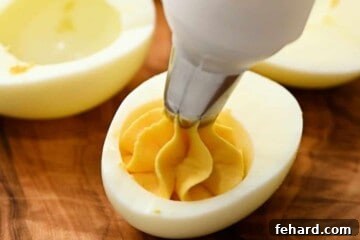 Irresistible Deviled Eggs 7 Piping bag piping filling deviled egg mixture into egg white.