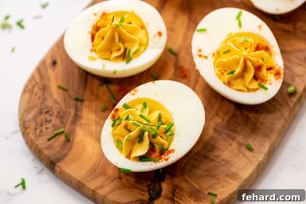 The Best Deviled Eggs Serving Three perfectly assembled deviled eggs, garnished with chives and paprika, resting on a small wooden platter, ready to be enjoyed.
