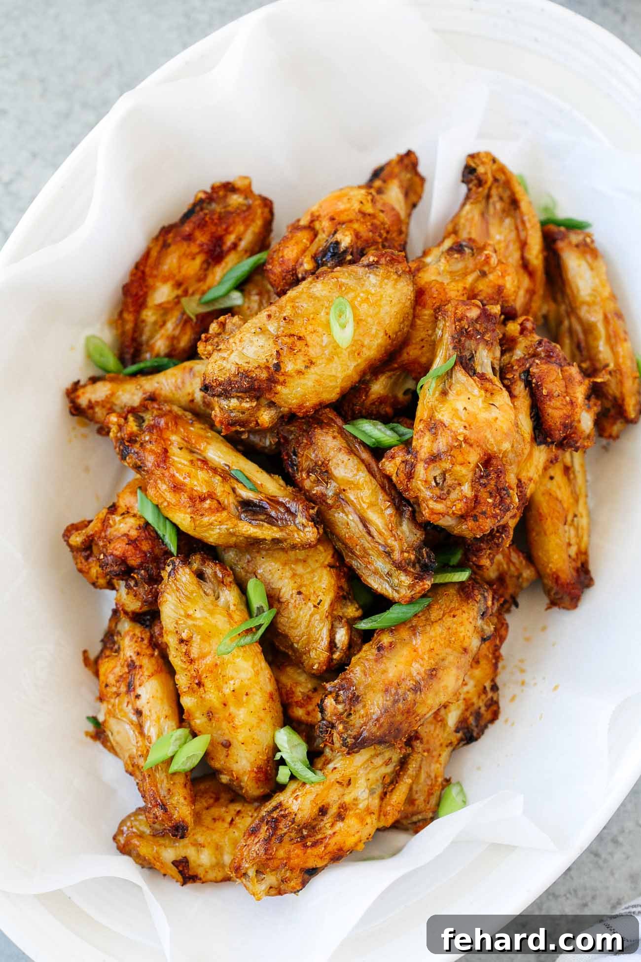 A white plate with chicken wings and green onion garnish.