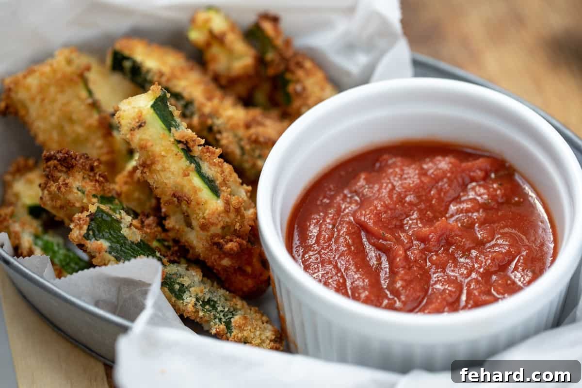 Air Fryer Zucchini Fries Basket of golden brown and crispy air fryer zucchini fries with a small bowl of marinara sauce for dipping.