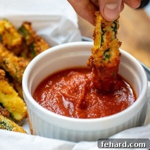 An Air Fryer Zucchini Fry being dipped into marinara sauce, highlighting its golden, crispy texture.