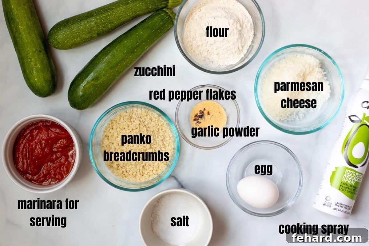 Air Fryer Zucchini Fries Recipe Individual ingredients for air fryer zucchini fries laid out on a white countertop: zucchini, flour, egg, panko breadcrumbs, grated parmesan cheese, garlic powder, and red pepper flakes.