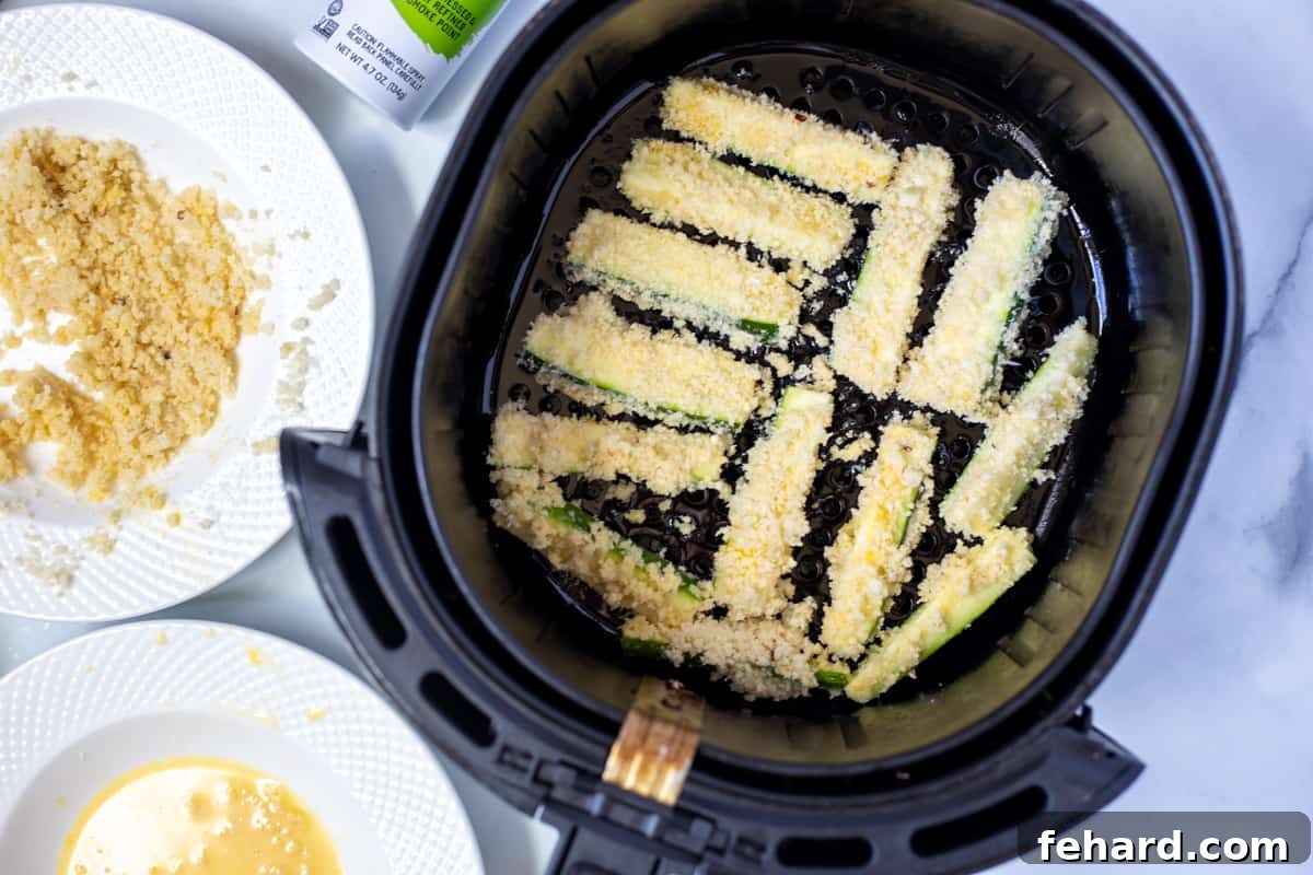 Low Fat Zucchini Fries A batch of breaded zucchini fries arranged neatly in the basket of an air fryer, ready for cooking.