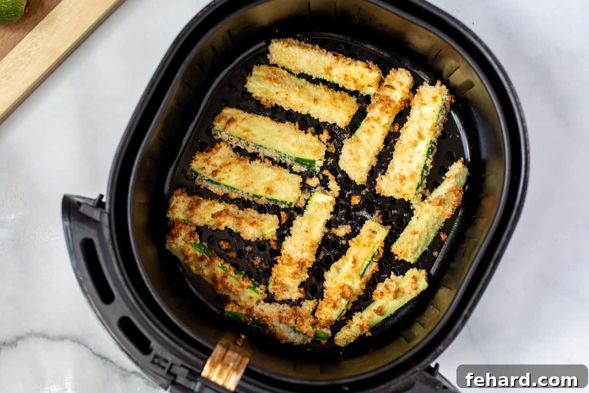 Breaded Zucchini Fries A close-up shot of golden, crispy air-fried zucchini fries in an air fryer basket, steam gently rising.