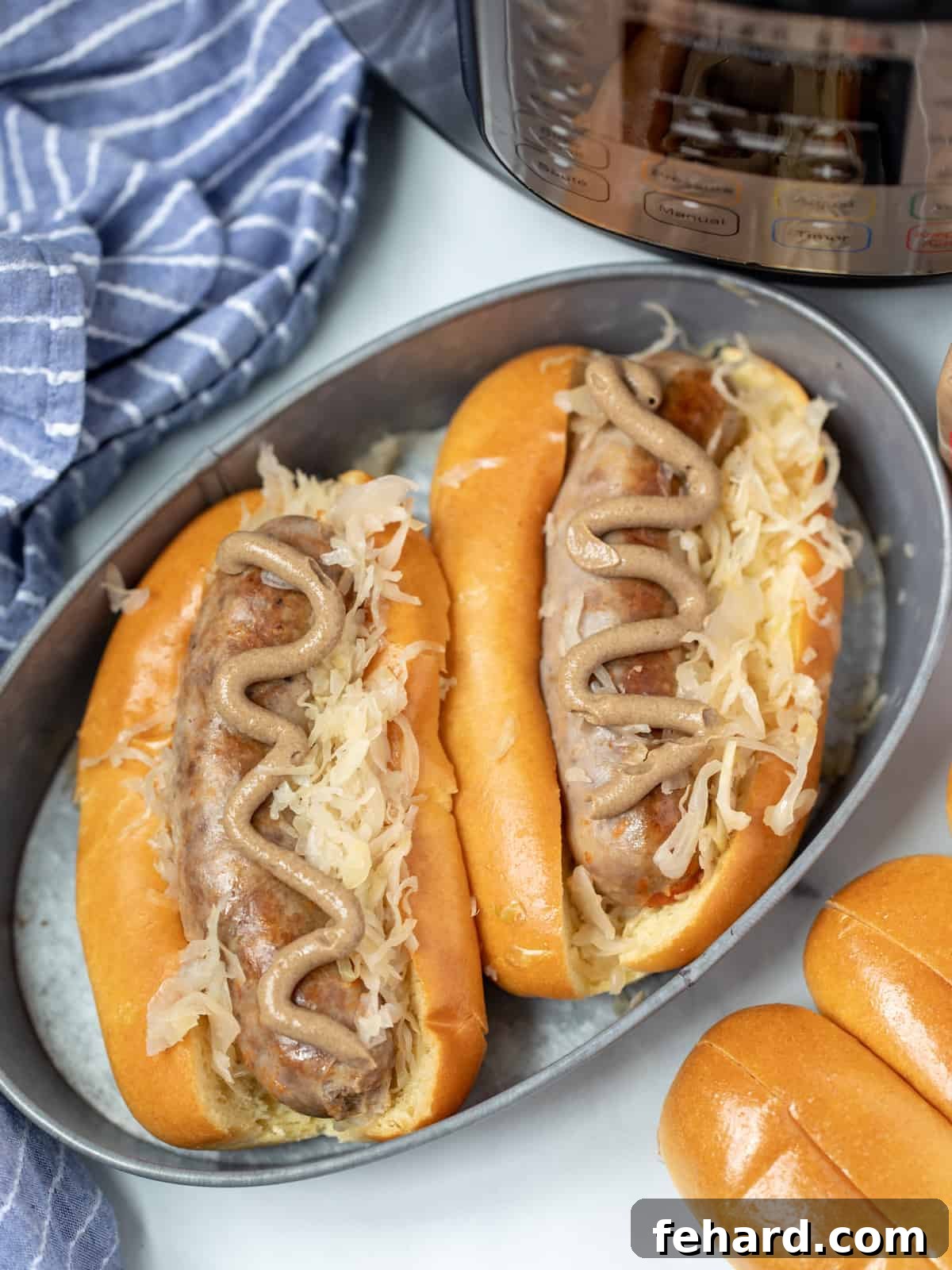 Two pressure cooked brats in buns with mustard and sauerkraut next to an Instant Pot. 