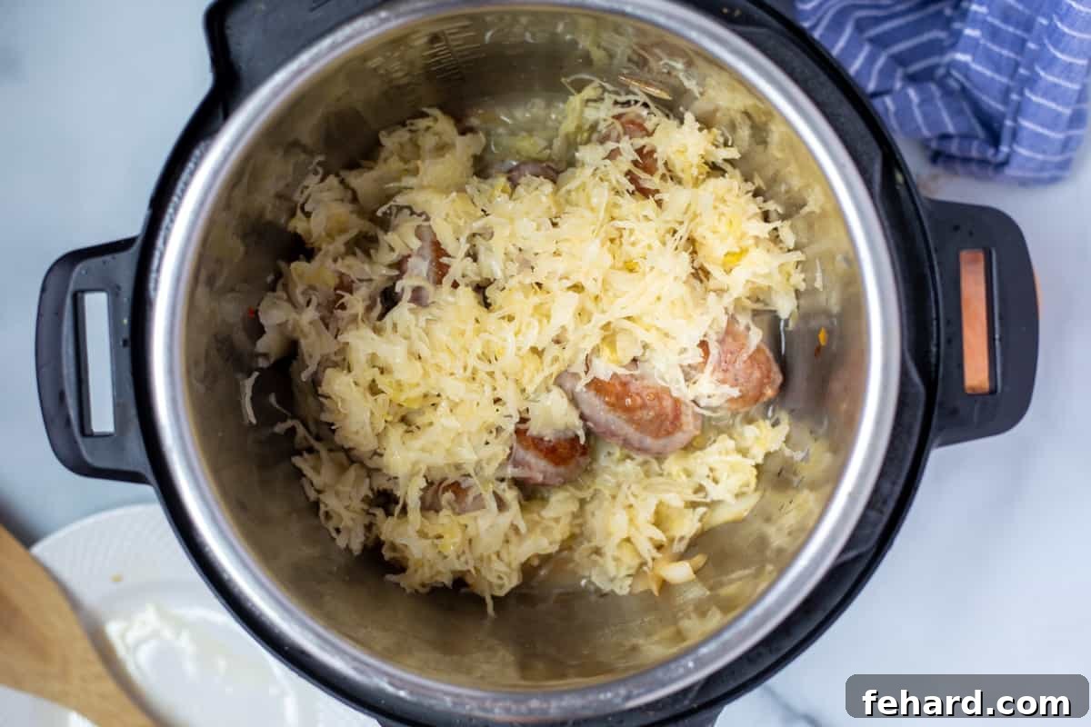 Brats with sauerkraut and onions layered in the inner pot of an Instant Pot, ready for pressure cooking.