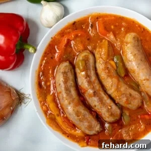 Sausage and Peppers in white serving dish next to peppers, garlic, and onions.