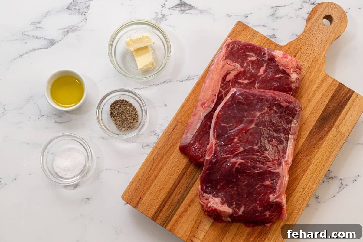 A selection of raw ribeye steaks, alongside a bottle of oil, a shaker of kosher salt, a pepper grinder, and a cube of butter, laid out on a clean wooden surface, ready for preparation.