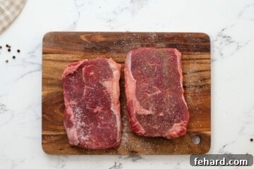 Two Seasoned Ribeye Steaks on cutting board.