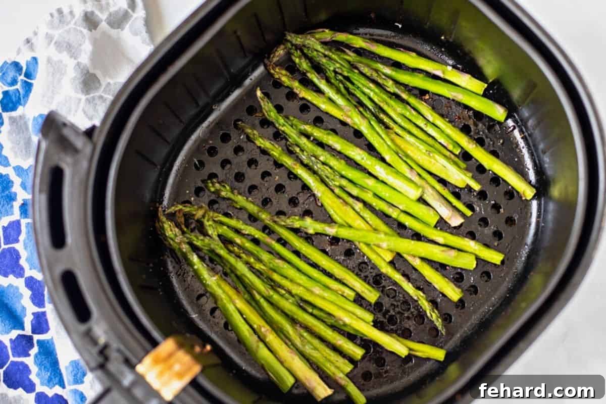 Seasoned asparagus spears perfectly arranged in a single layer inside an air fryer basket, ready to be cooked.