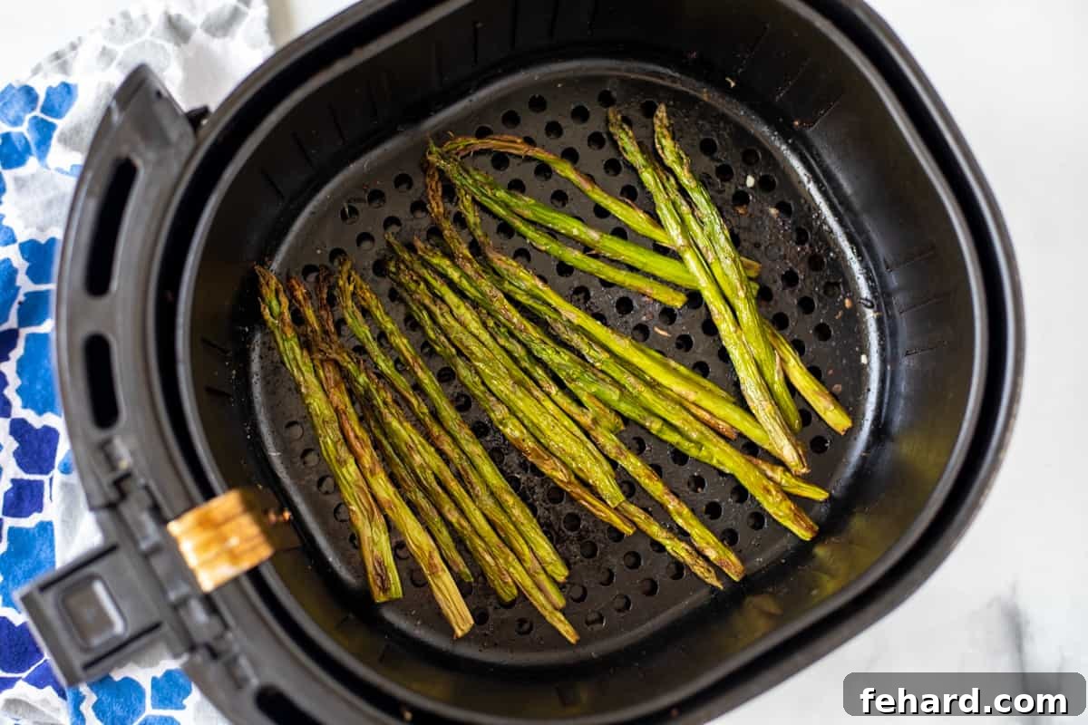 Perfectly roasted asparagus, golden and slightly charred, resting in the air fryer basket immediately after cooking.