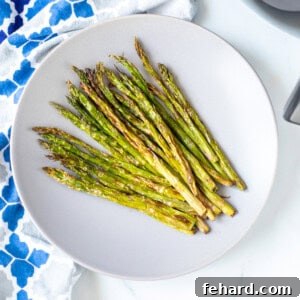 A plate of crispy asparagus next to air fryer, showcasing the delicious result.