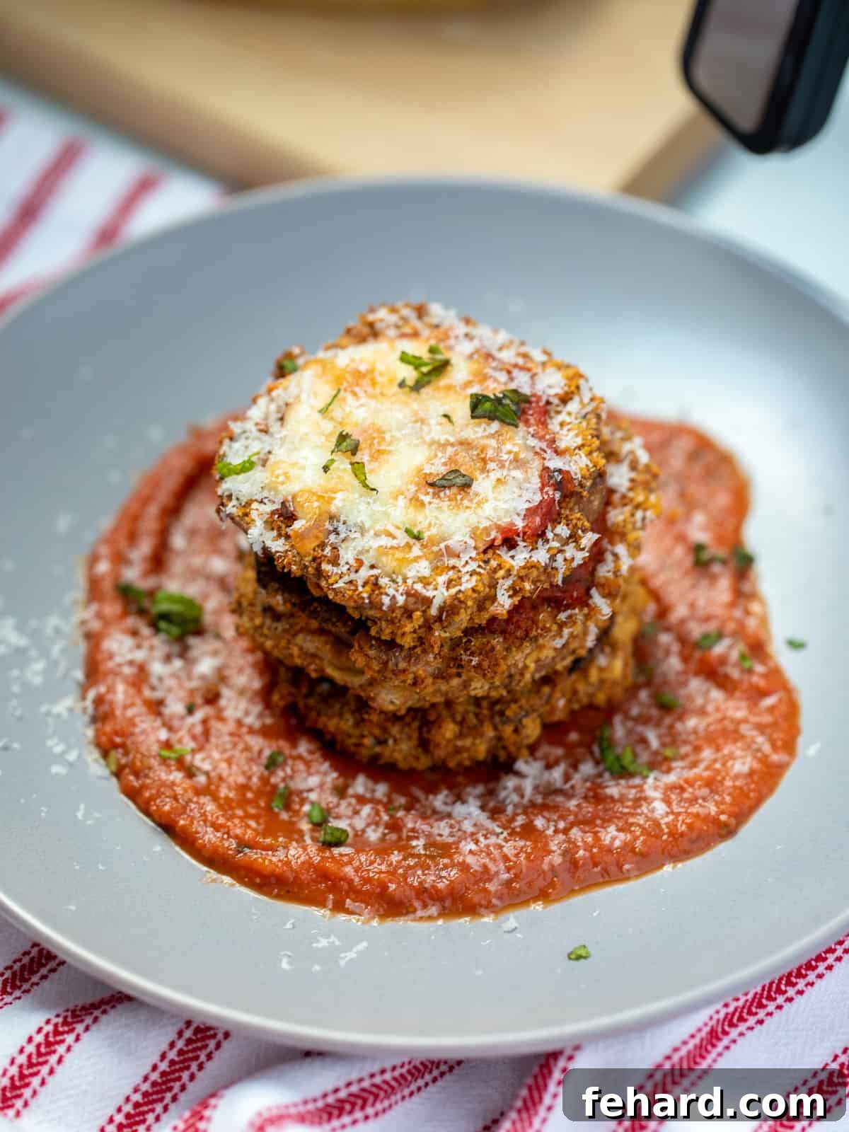 Stack of golden-brown, crispy Air Fryer Eggplant Parmesan slices on a gray plate, garnished with fresh basil and grated Parmesan cheese.