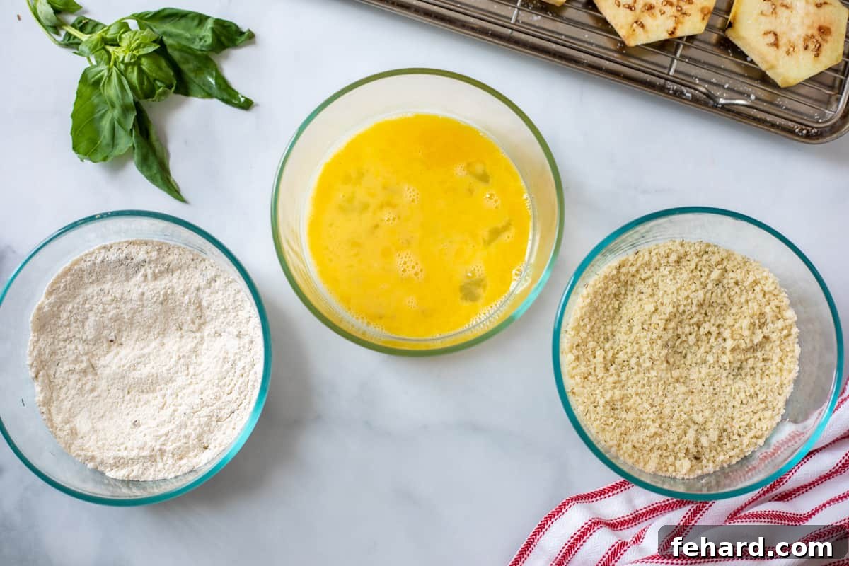 Three shallow dishes set up for a breading station, containing seasoned flour, whisked egg wash, and a flavorful panko-Parmesan mixture.