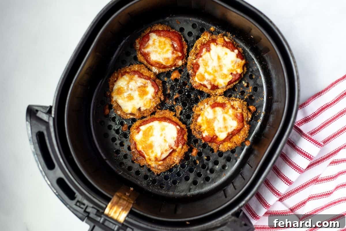 Crispy air-fried eggplant parmesan slices with melted mozzarella and rich marinara sauce, fresh out of the air fryer basket, ready to serve.
