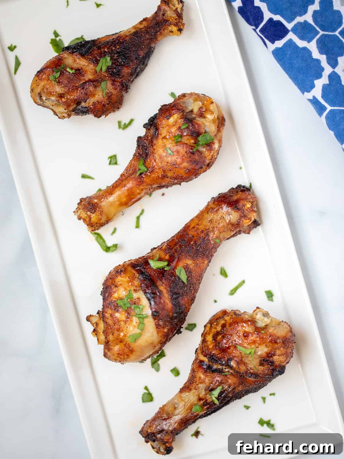 Four Air Fryer Chicken Legs that have been rubbed with a sweet and smoky dry rub and air fried until tender and juicy on a white platter. 