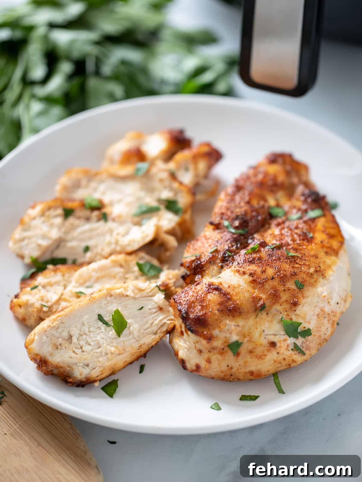 Two golden brown, spice-rubbed air fryer chicken breasts on a white platter, garnished with fresh herbs, next to a modern black air fryer.