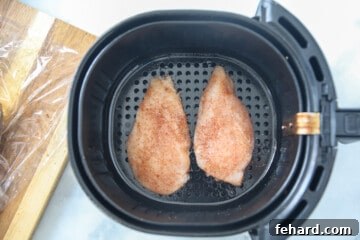 Two seasoned chicken breasts placed in a preheated air fryer basket, ready to cook.