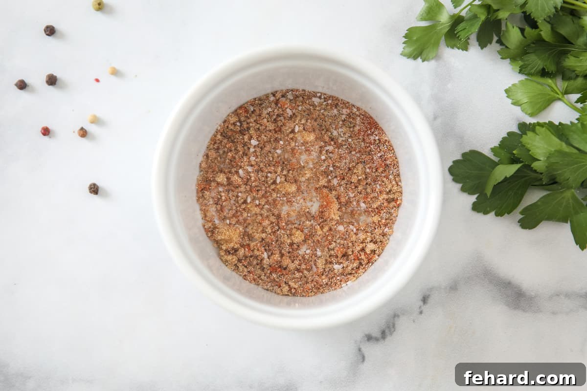 A small white bowl filled with a reddish-brown spice rub, including visible specks of paprika, garlic powder, and herbs, ready for chicken seasoning.