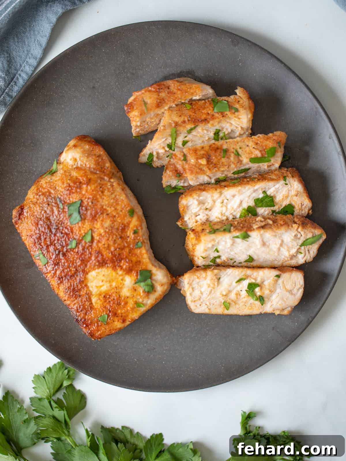 Two golden-brown, juicy Air Fryer Pork Chops on a gray plate, garnished with fresh herbs.