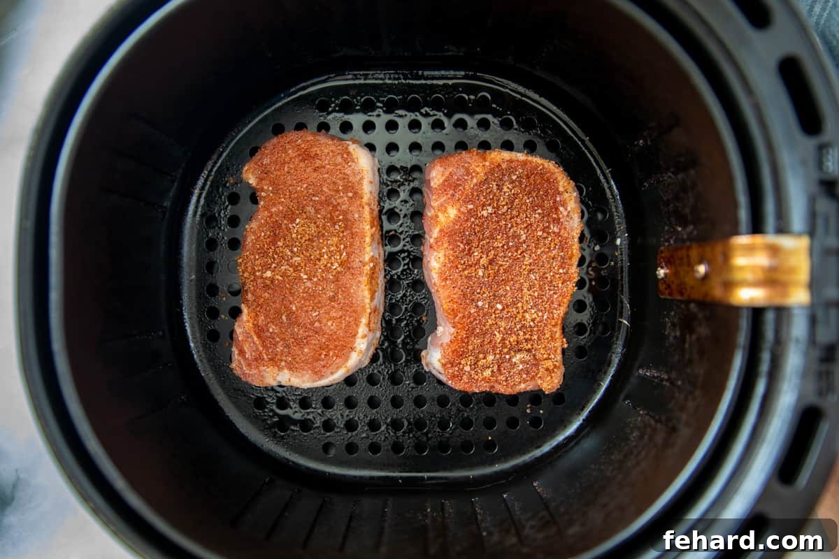 Two perfectly seasoned pork chops arranged in a single layer within an air fryer basket.