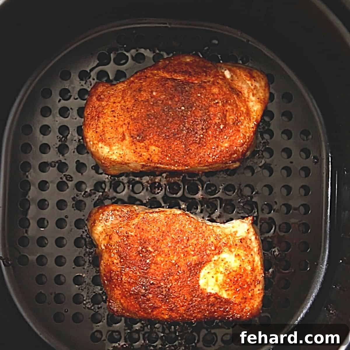 Freshly air-fried pork chops with a golden crust inside an air fryer basket.