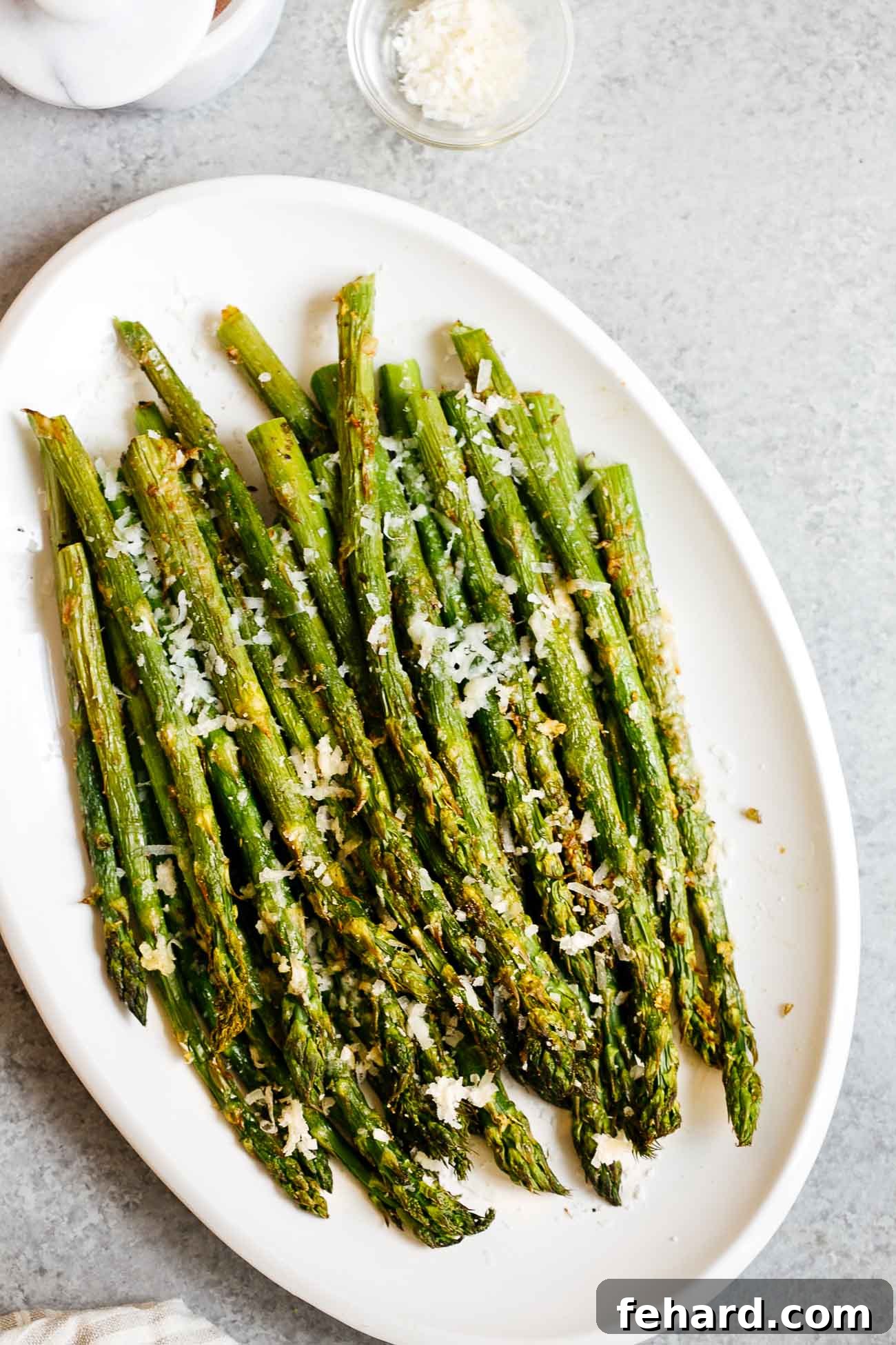 Vibrant green asparagus spears perfectly cooked in an air fryer, scattered with Parmesan cheese, presented in an overhead view on a rustic plate.
