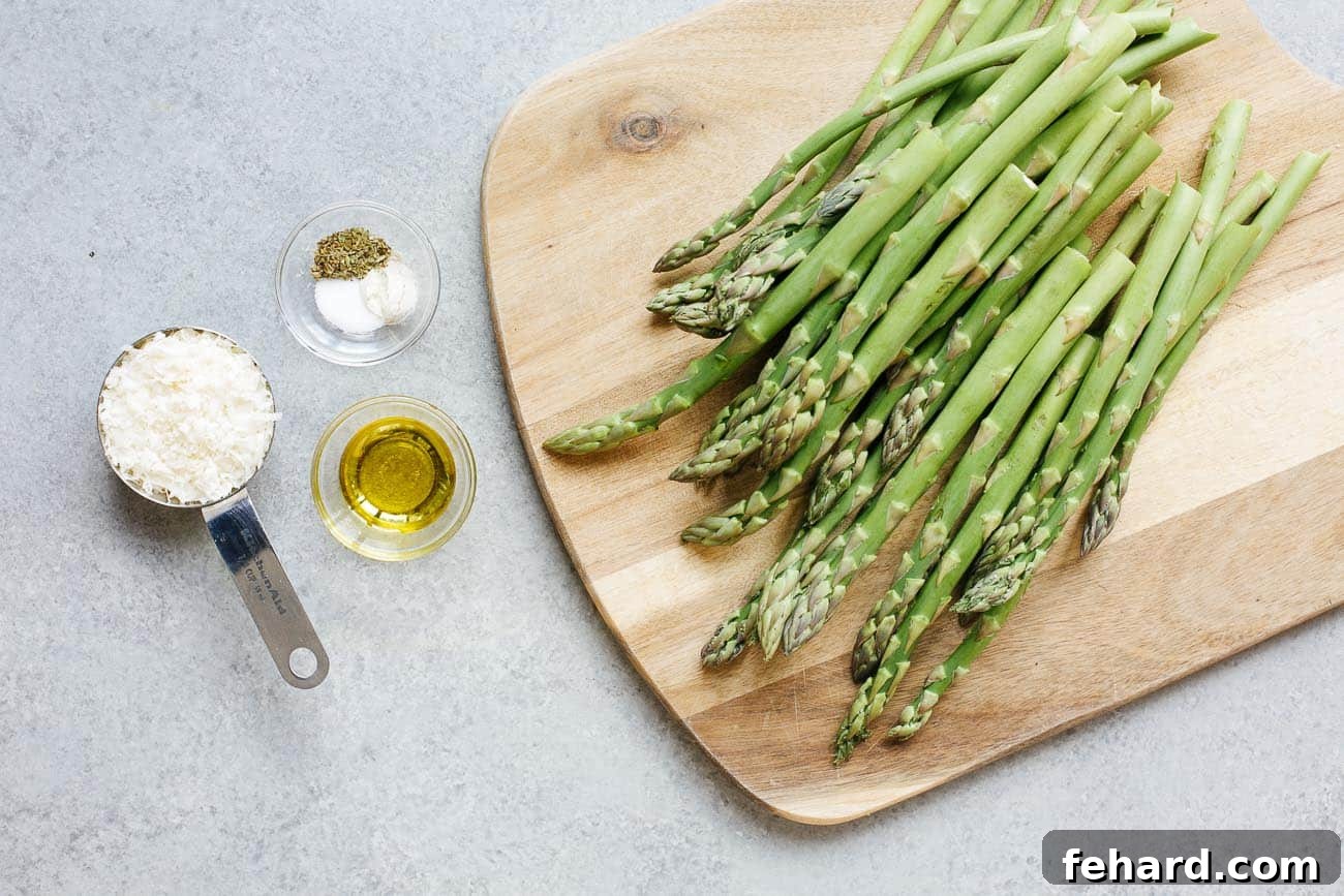 Close-up overhead shot of the simple ingredients laid out for air fryer asparagus: fresh green asparagus spears, a bowl of grated Parmesan cheese, olive oil, and salt and pepper.