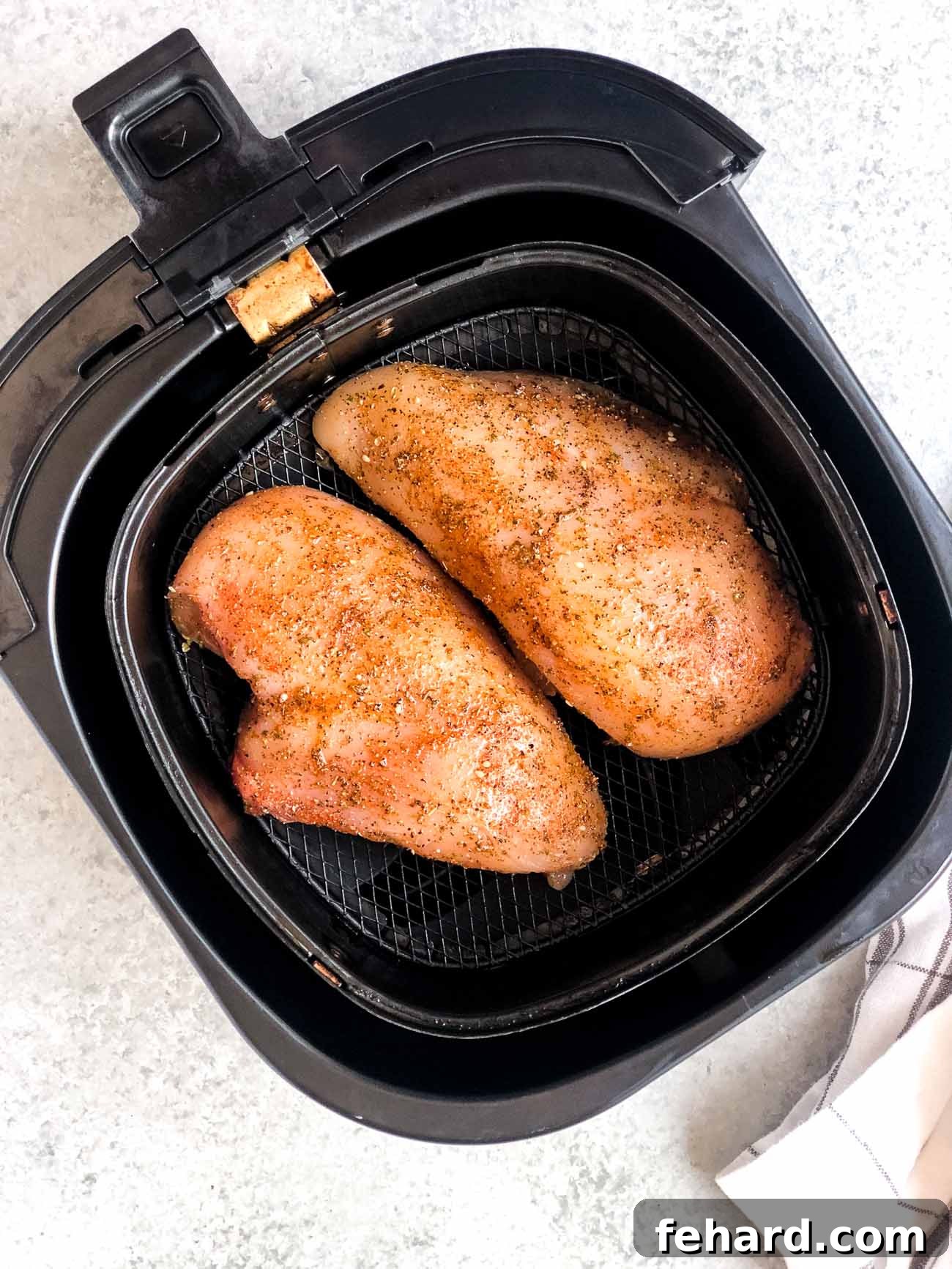raw and seasoned chicken breast inside of an air fryer basket