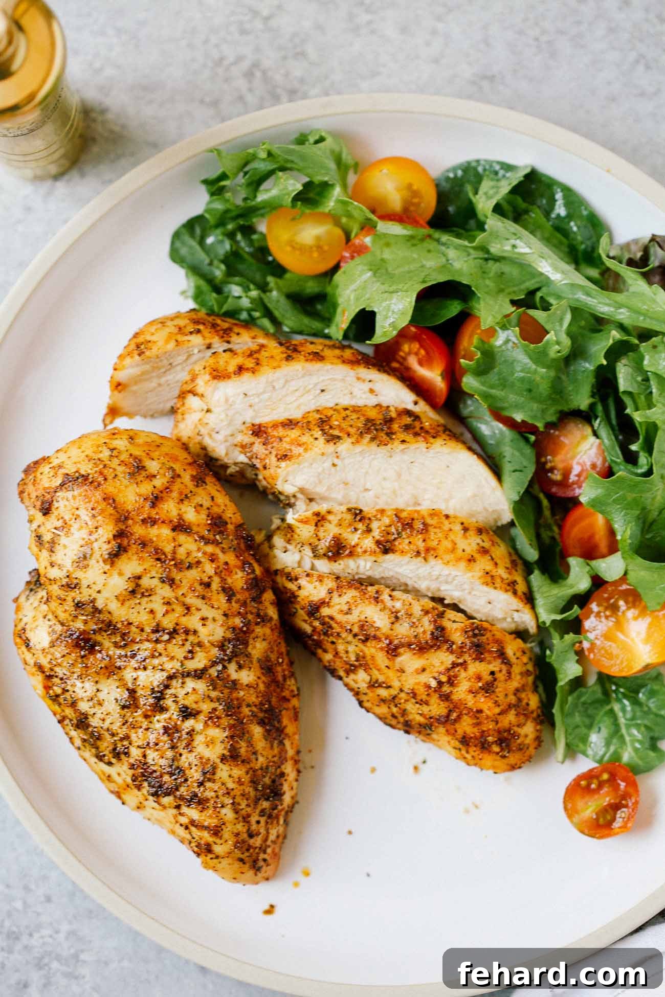 A plate with two chicken breasts, one sliced, beside a salad.