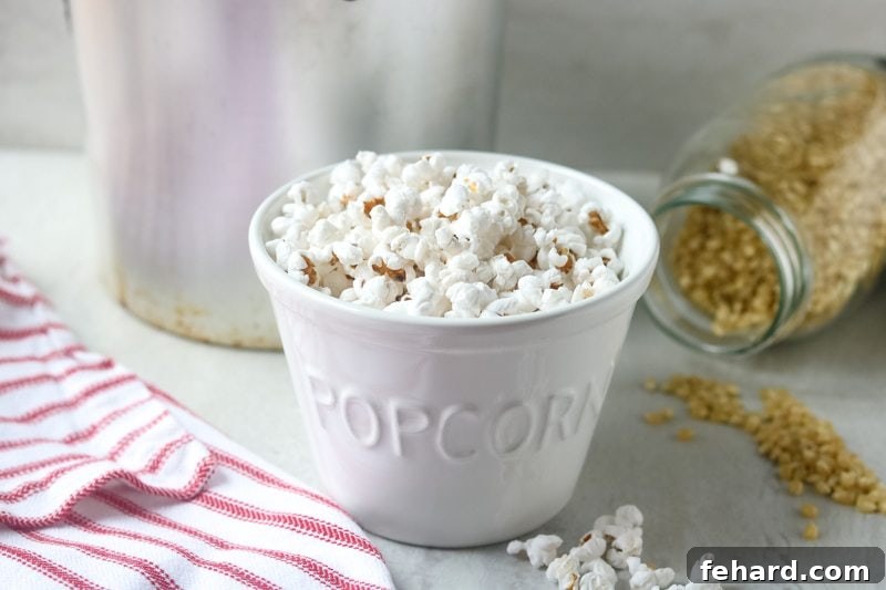 Stovetop Popcorn Recipe Freshly made stovetop popcorn in a white bowl with a popcorn popper in the background.