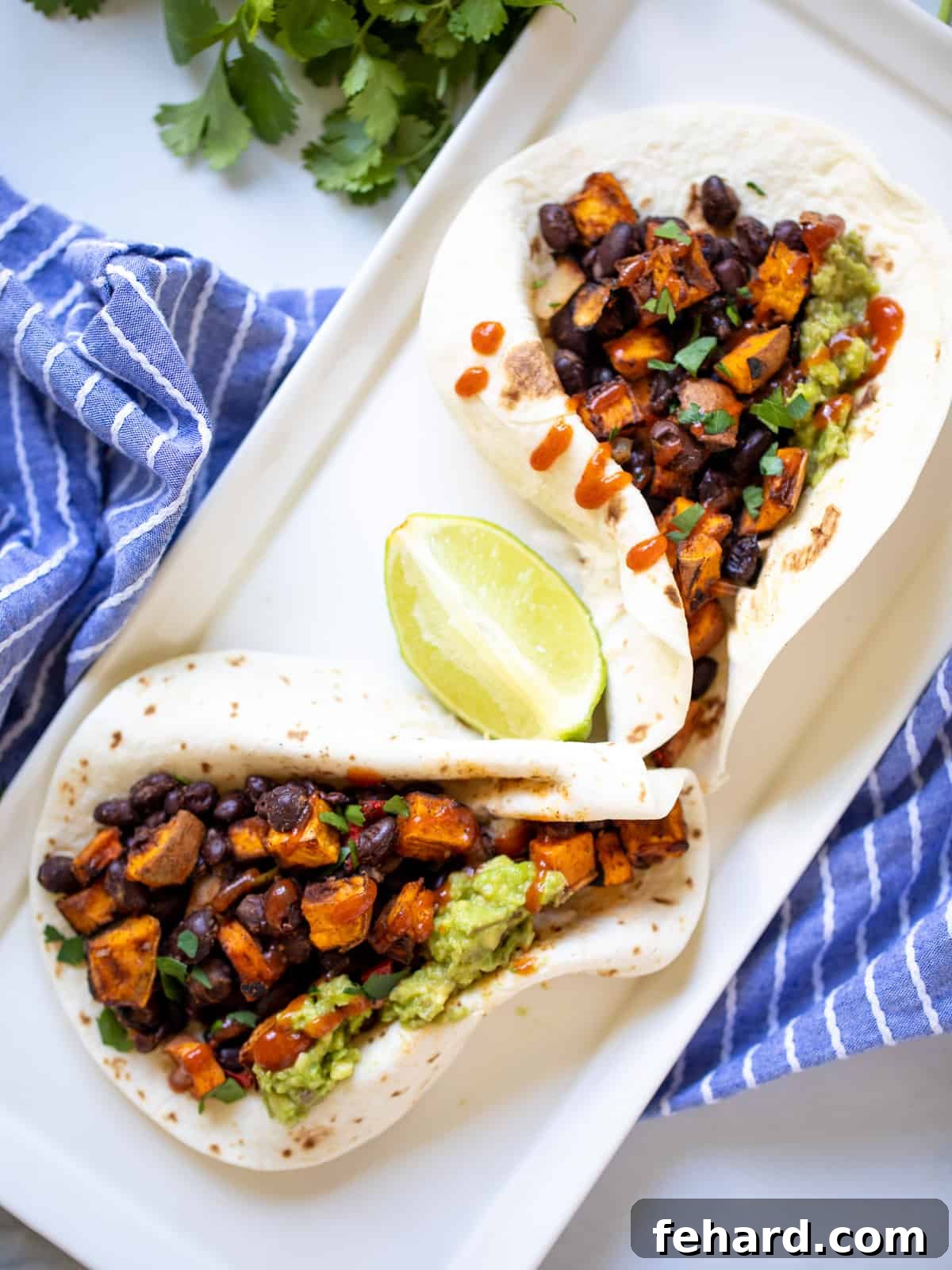 Two flour tortillas filled with colorful sweet potatoes, black beans, and creamy guacamole, ready to be enjoyed.