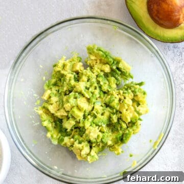 Mashed avocado in bowl with whole avocado next to it.