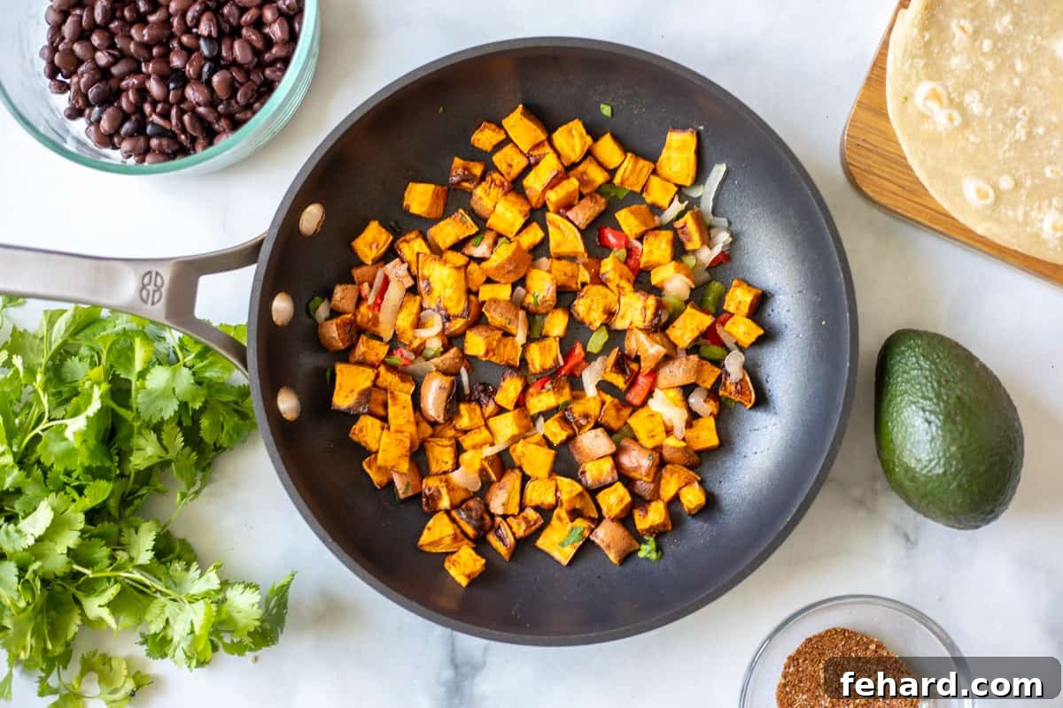 Sautéed sweet potatoes, bell peppers, and onions cooking in a skillet, with black beans and cilantro waiting nearby.