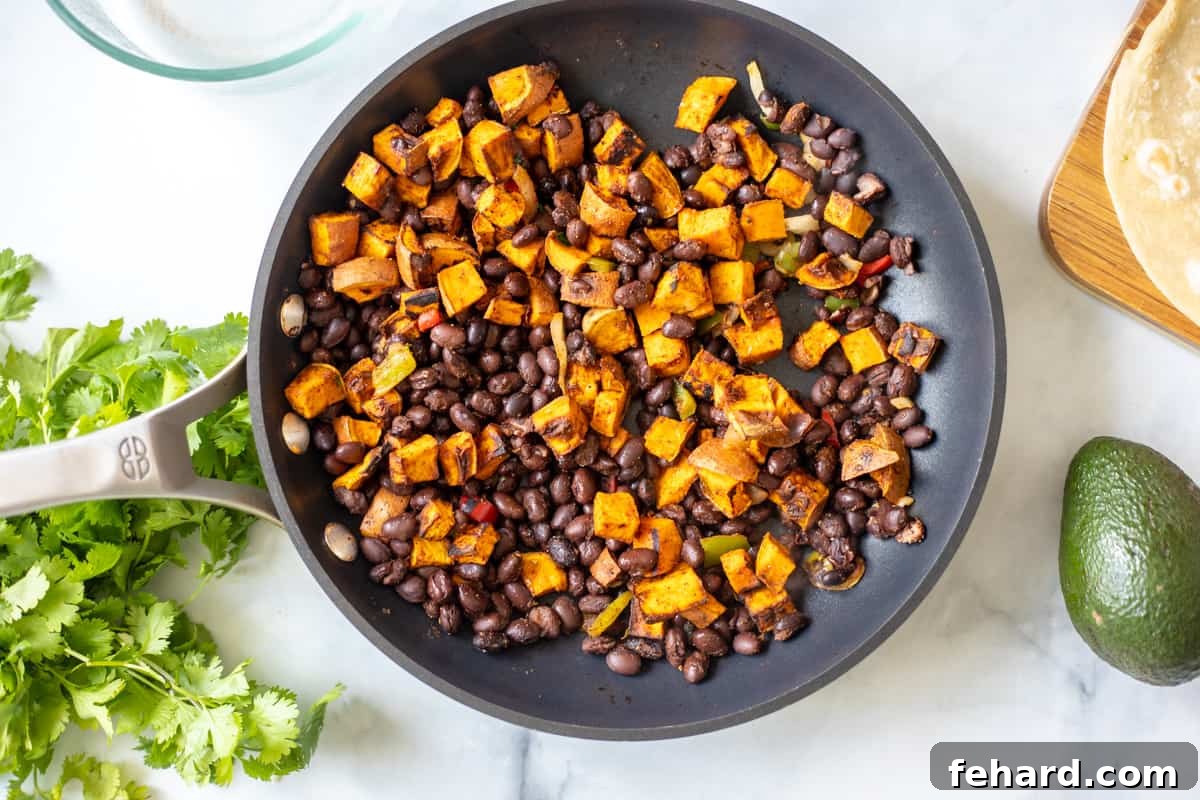A close-up of the sweet potato and black bean filling simmering in a skillet, seasoned with spices, forming the core of a delicious vegetarian taco.