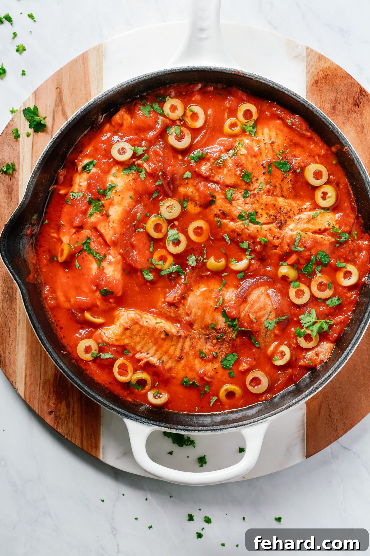 Close-up view of the cooked tilapia and tomato-onion sauce in a white skillet, ready to be served.