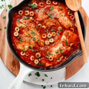 Overhead view of a white skillet containing tilapia in a tomato sauce.