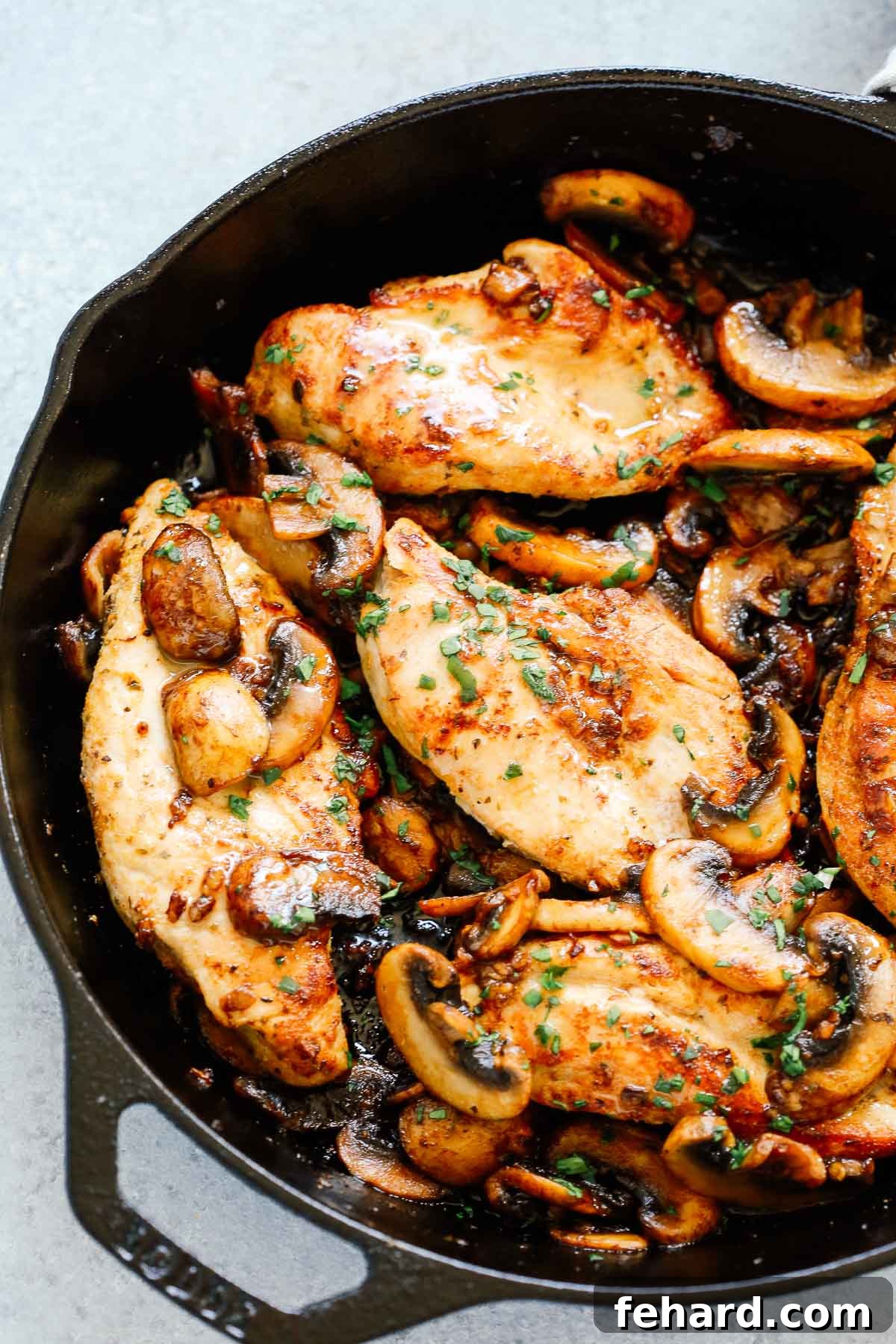 close up of mushrooms and chicken breast topped with fresh parsley in a skillet