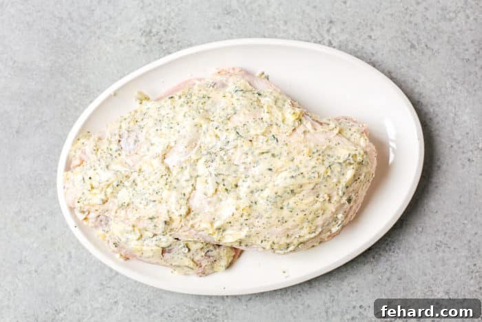 A turkey breast generously coated with the garlic butter mixture both under and over the skin, ready for roasting.